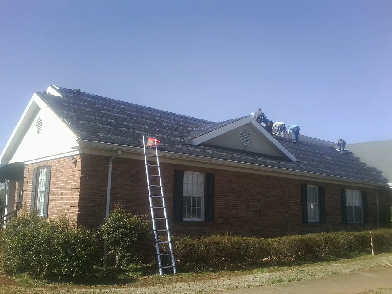 Crew tearing shingles off a brick ranch roof with a ladder set — Emergency Roof Repair work by our crew in Grand Junction