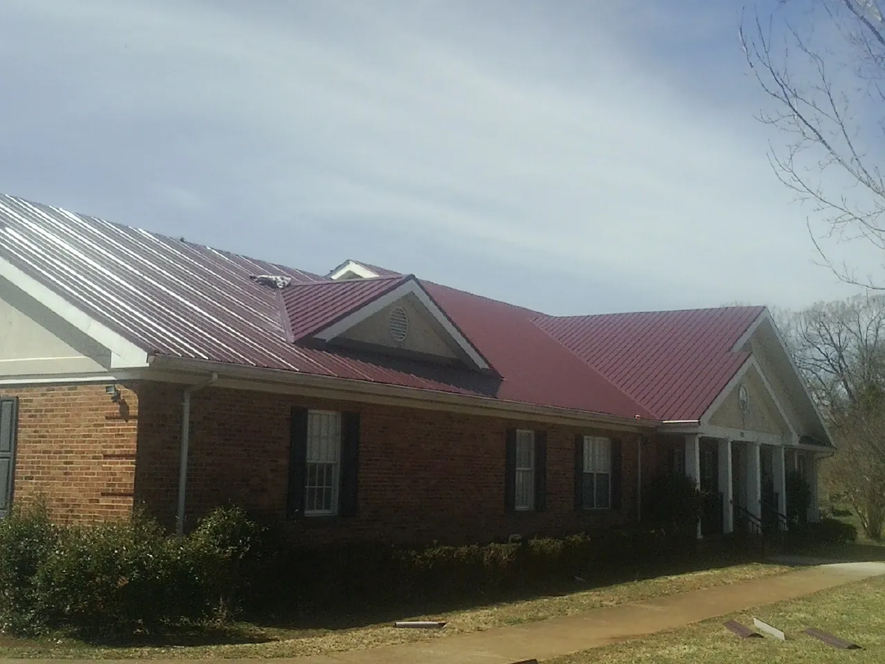 Red metal roof with gabled entries on a long brick building, from a Hail Damage Roof Repair job in Grand Junction